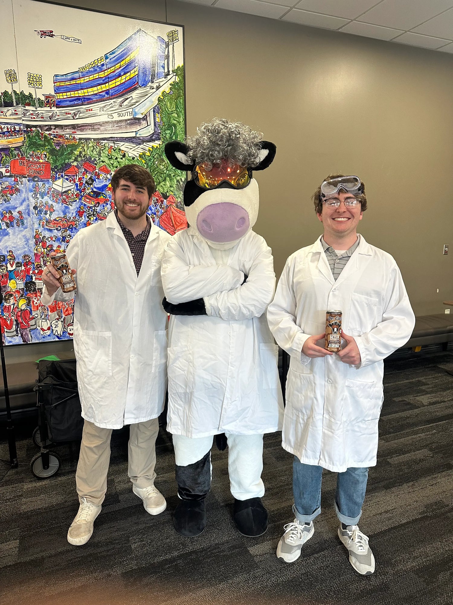 Two people in lab coats (Tyler & Lee) with a cow mascot (Dr. Cal)